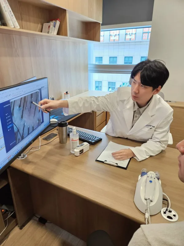모니터에 확대된 두피 이미지를 가리키며 설명하는 탈모 전문 의사